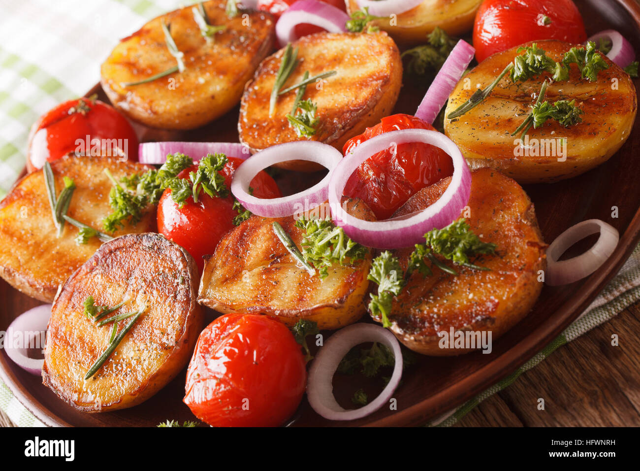Cibo vegetariano: grigliate di nuovo le patate e pomodori con rosmarino macro su una piastra sul tavolo orizzontale. Foto Stock