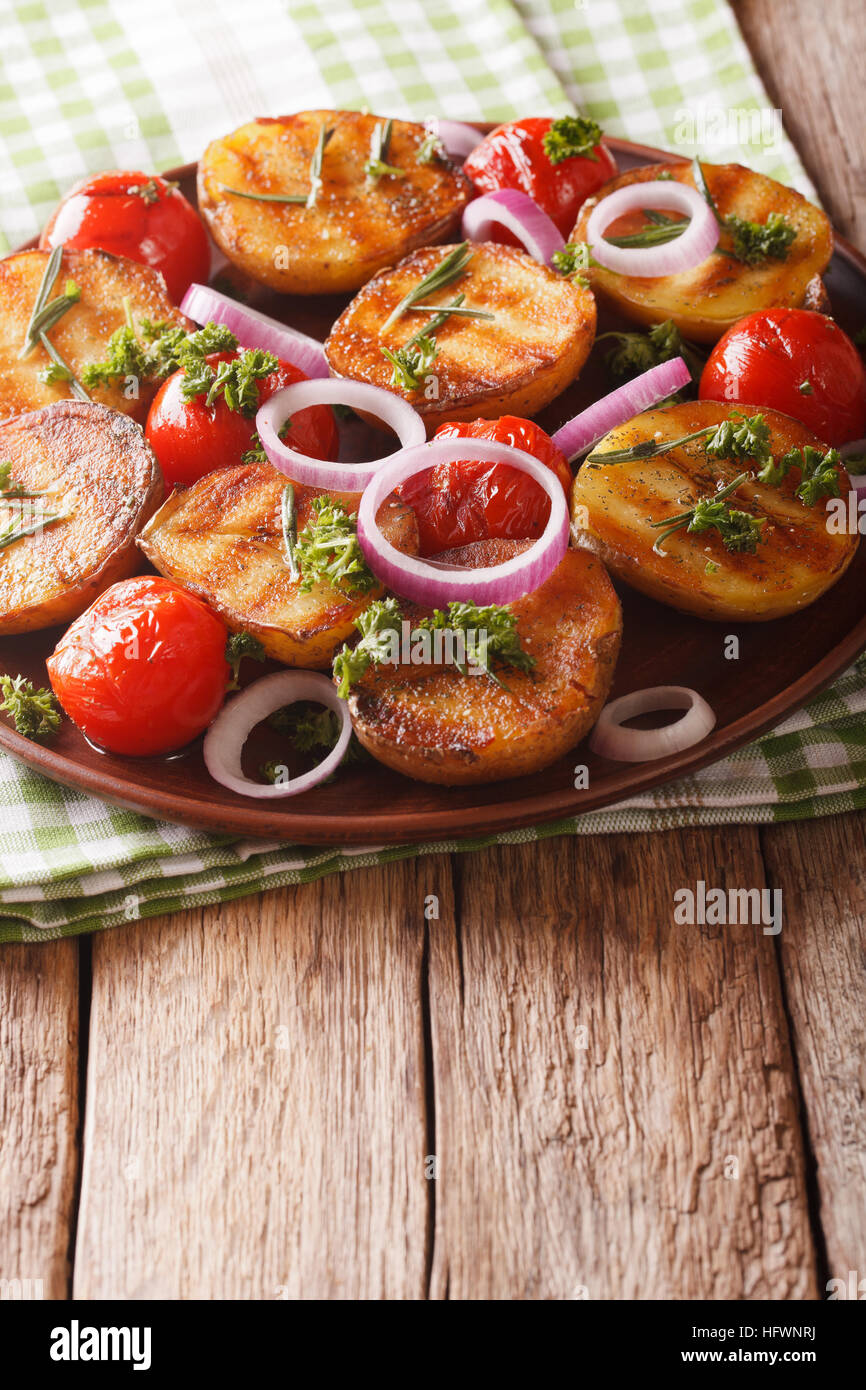 Cibo vegetariano: grigliate di nuovo le patate e pomodori con rosmarino close up su una piastra sul piano verticale. Foto Stock