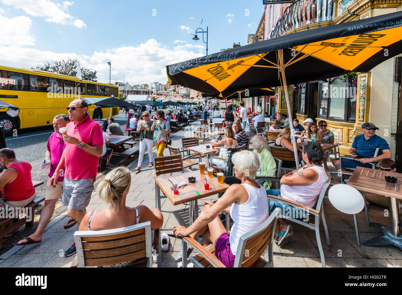 Lungomare di inglese a Ramsgate con persone sedute a tavoli e sedie sotto gli ombrelloni e gustare drinks durante il tempo molto caldo in estate. Foto Stock