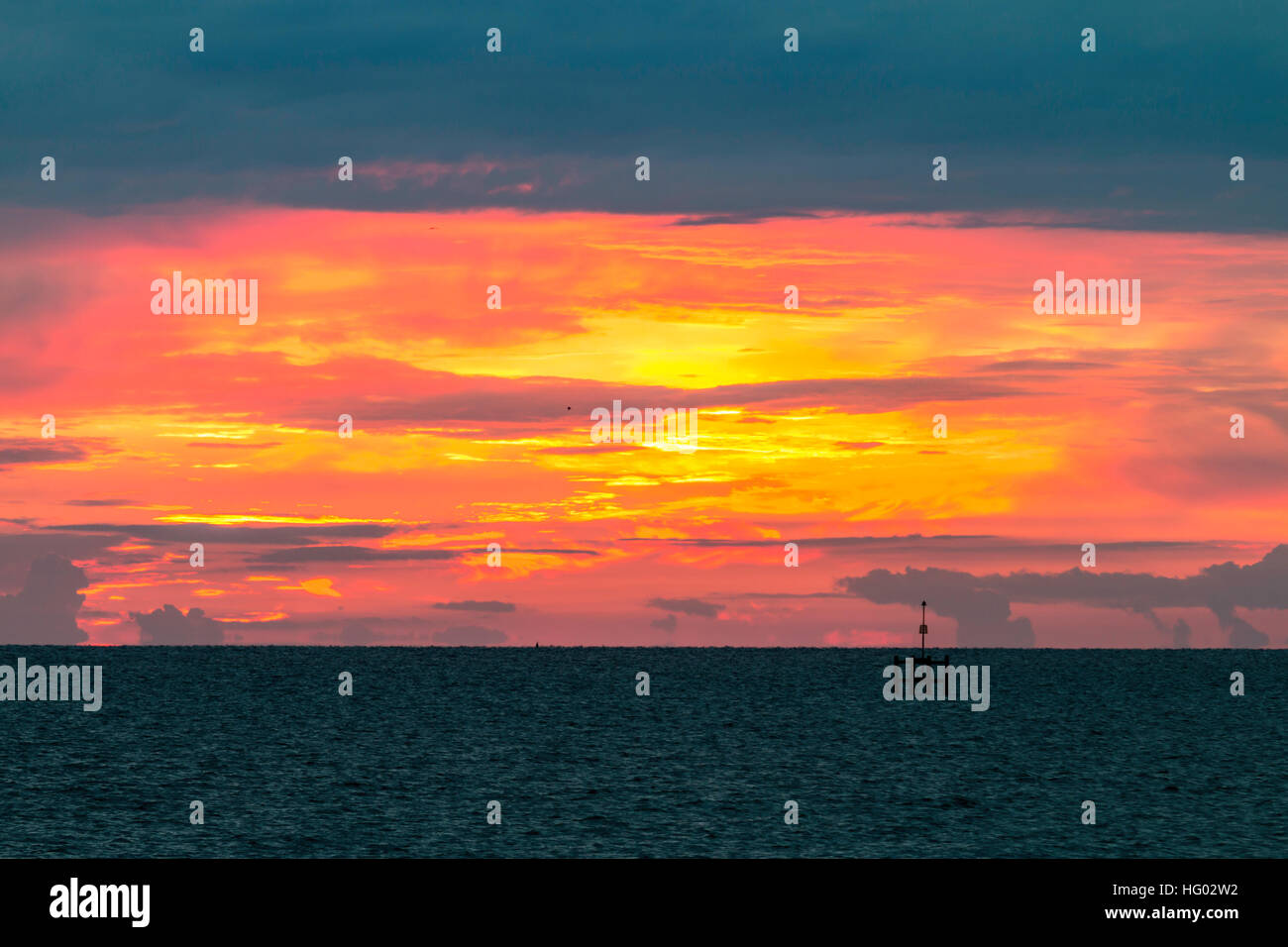 Inghilterra, Herne Bay. Canale Inglese a day break, drammatica di arancione e giallo sul cielo orizzonte con nuvole scure sopra. Bouy in primo piano. Foto Stock