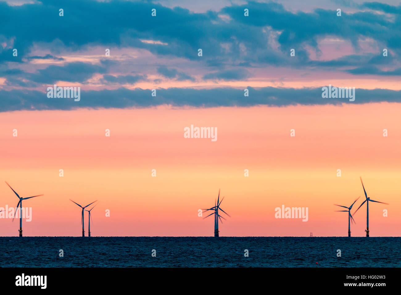 Inghilterra, Herne Bay. Le turbine eoliche, Kentish Flats per centrali eoliche nel Canale della Manica a day break, arancione chiaro cielo sull'orizzonte con le nuvole scure sopra. Foto Stock
