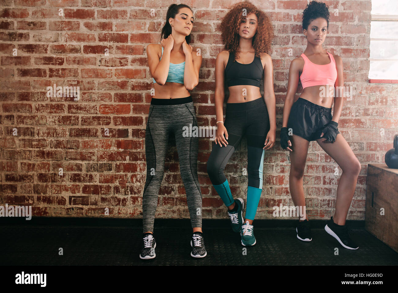 Ritratto di donna fitness abbigliamento sportivo in piedi contro un muro di mattoni in palestra. Gruppo multirazziale delle femmine in piedi insieme in un club salute. Foto Stock