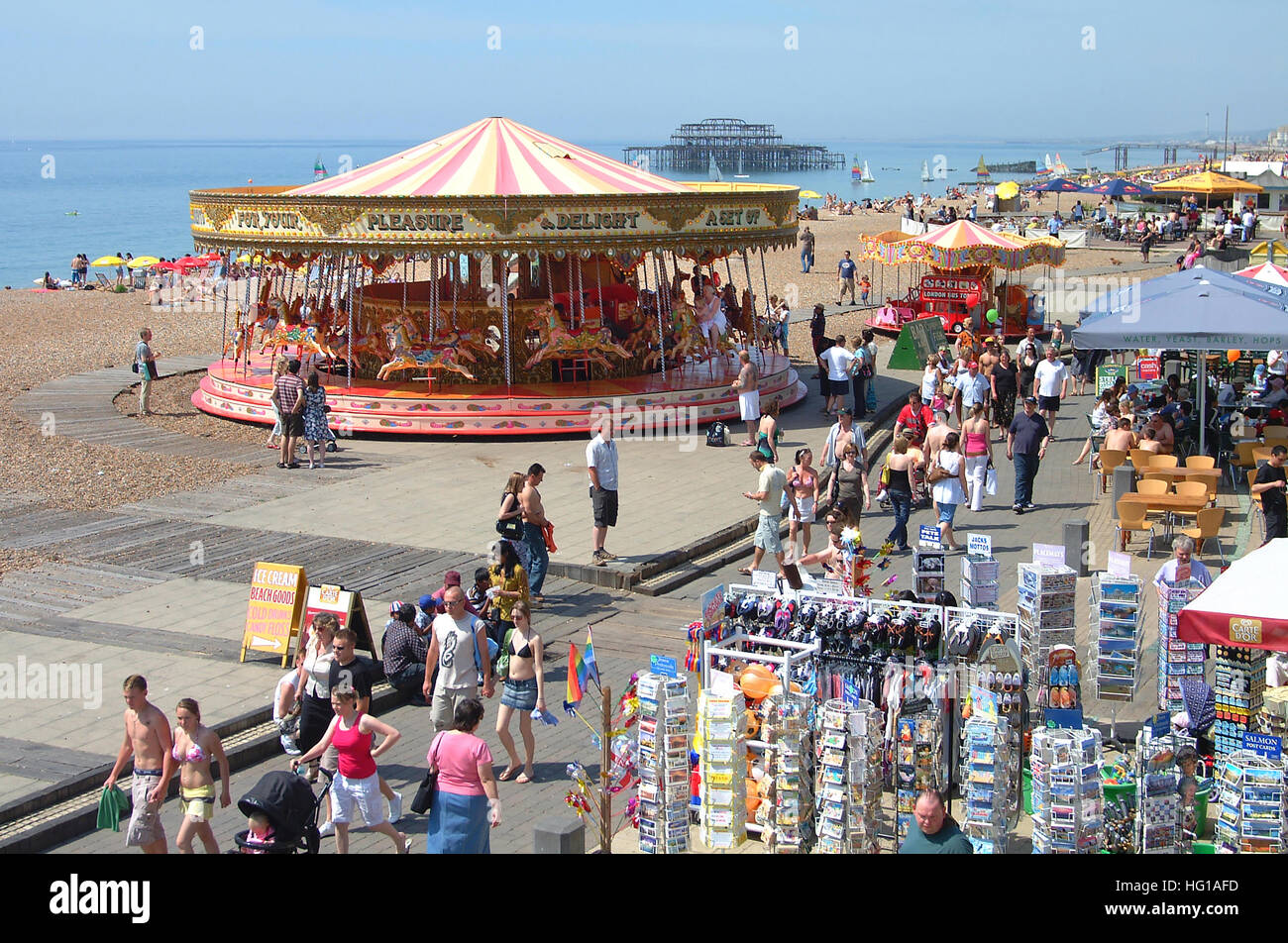 Le persone sul lungomare di Brighton, cartoline. persone, giostra, cafe e i resti del vecchio molo Ovest, vista dalla passeggiata sopra. Foto Stock