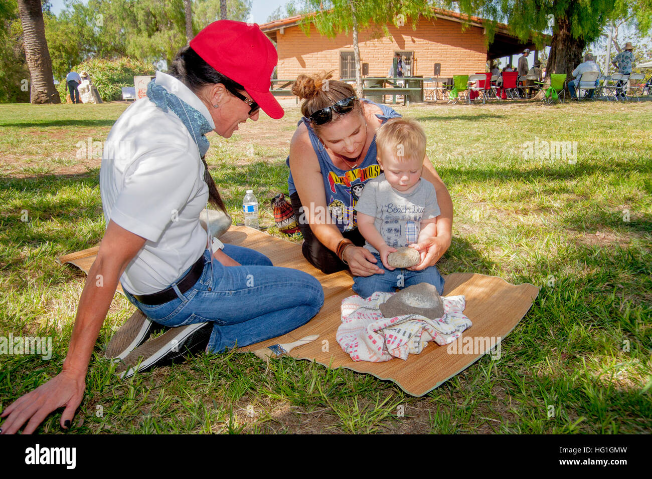 Un ragazzo impara antica Native American pietra macinazione di grano da un volontario in un "Early California giorni di festival in un parco in Costa Mesa, CA. Foto Stock