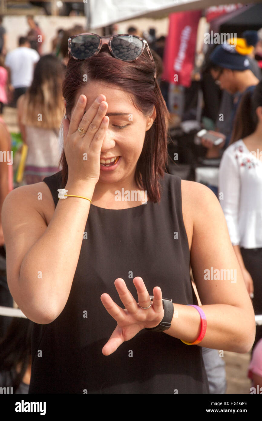 Un felice ma sorpreso giovane donna occhi la sua fidanzata di anello di fidanzamento sul suo dito dopo aver accettato la sua proposta in Huntington Beach, CA. Foto Stock