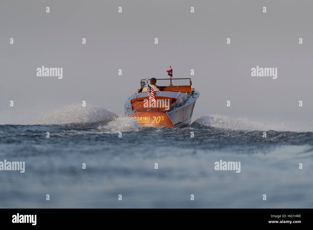 Un uomo che si allontana in un antico motoscafo in legno su un lago tranquillo. Foto Stock