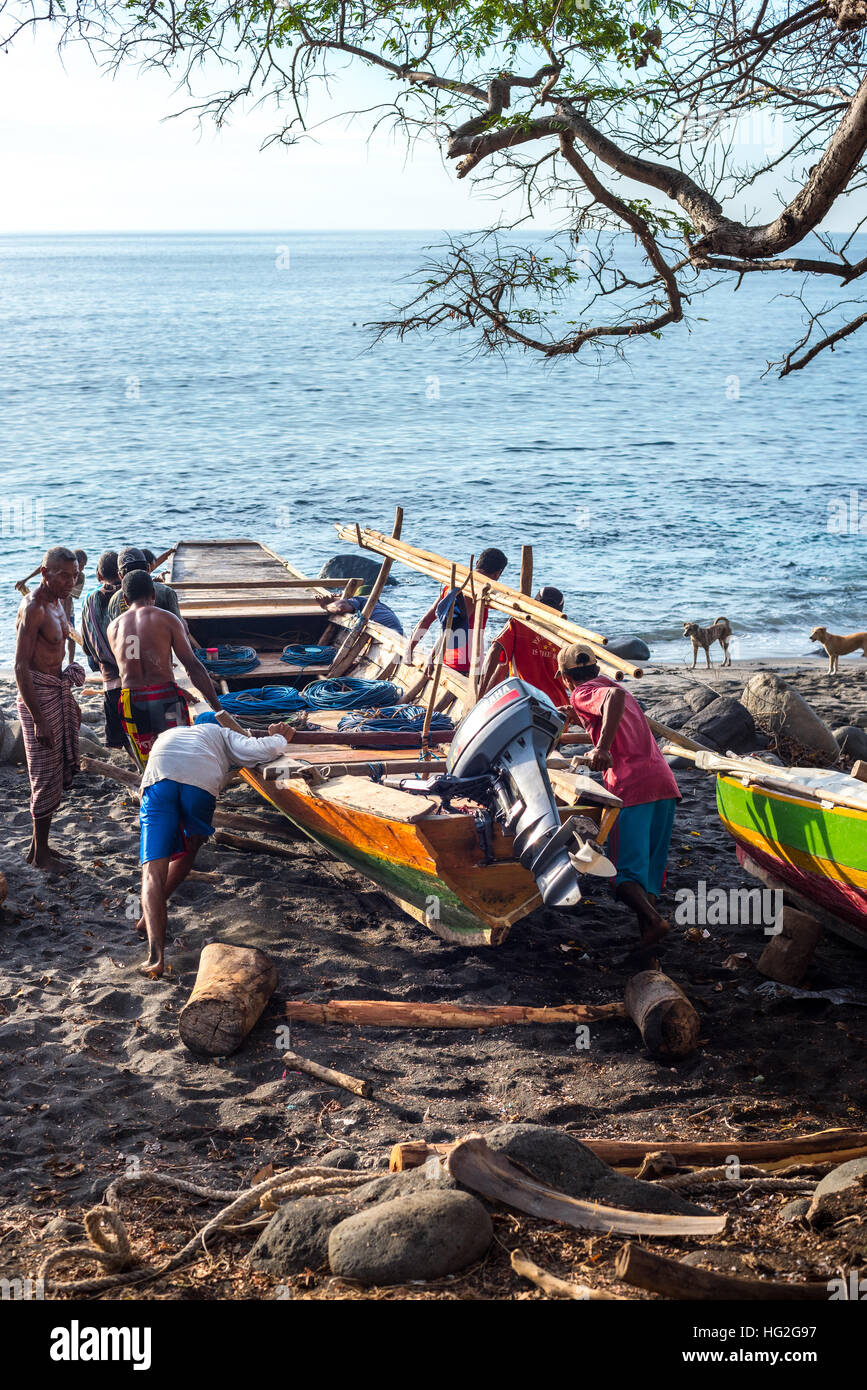 Un gruppo di pescatori spingendo la loro imbarcazione in legno nell'acqua di mare. Foto Stock
