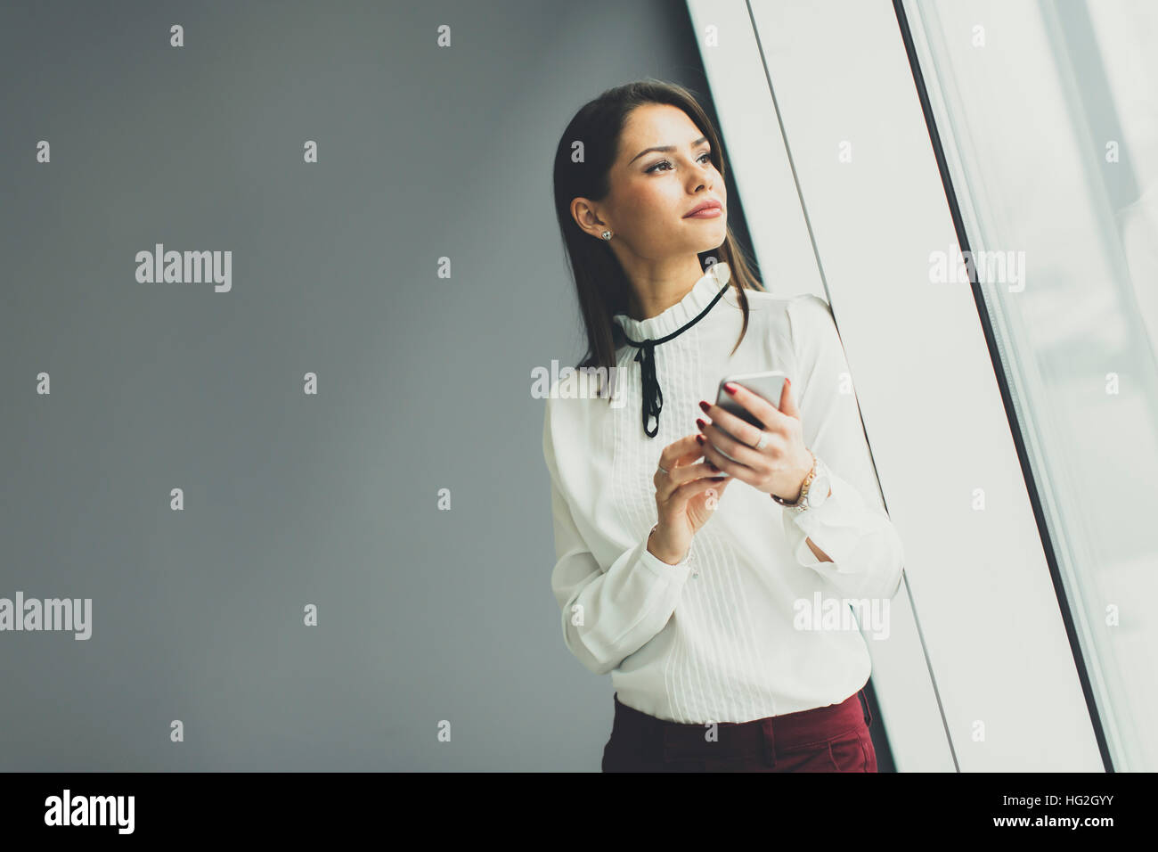 Piuttosto giovane donna con il cellulare da muro grigio in ufficio Foto Stock