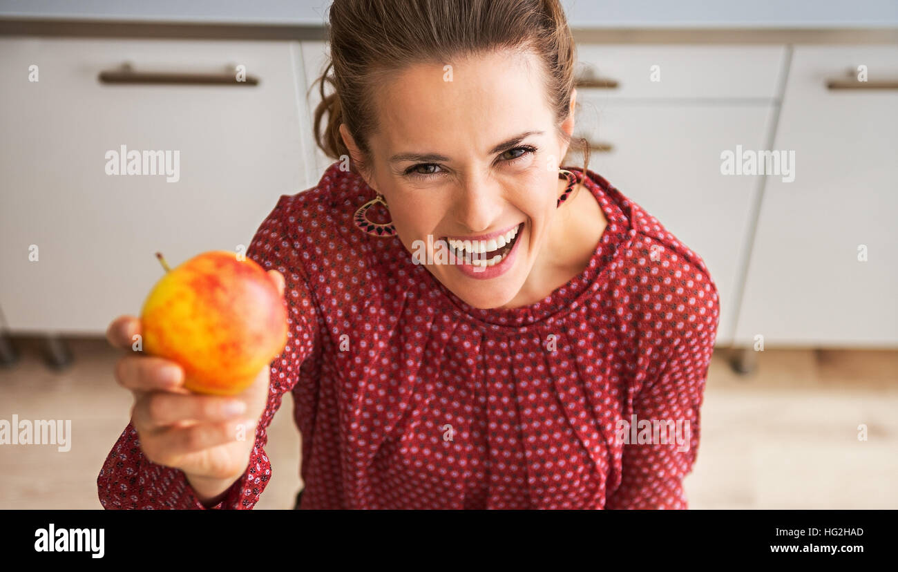 Prendere un boccone, prometto è deliziosa... Un elegante donna è ridere e stimolazione in una cucina, tenendo alto colorato apple e cullano una tela sac Foto Stock