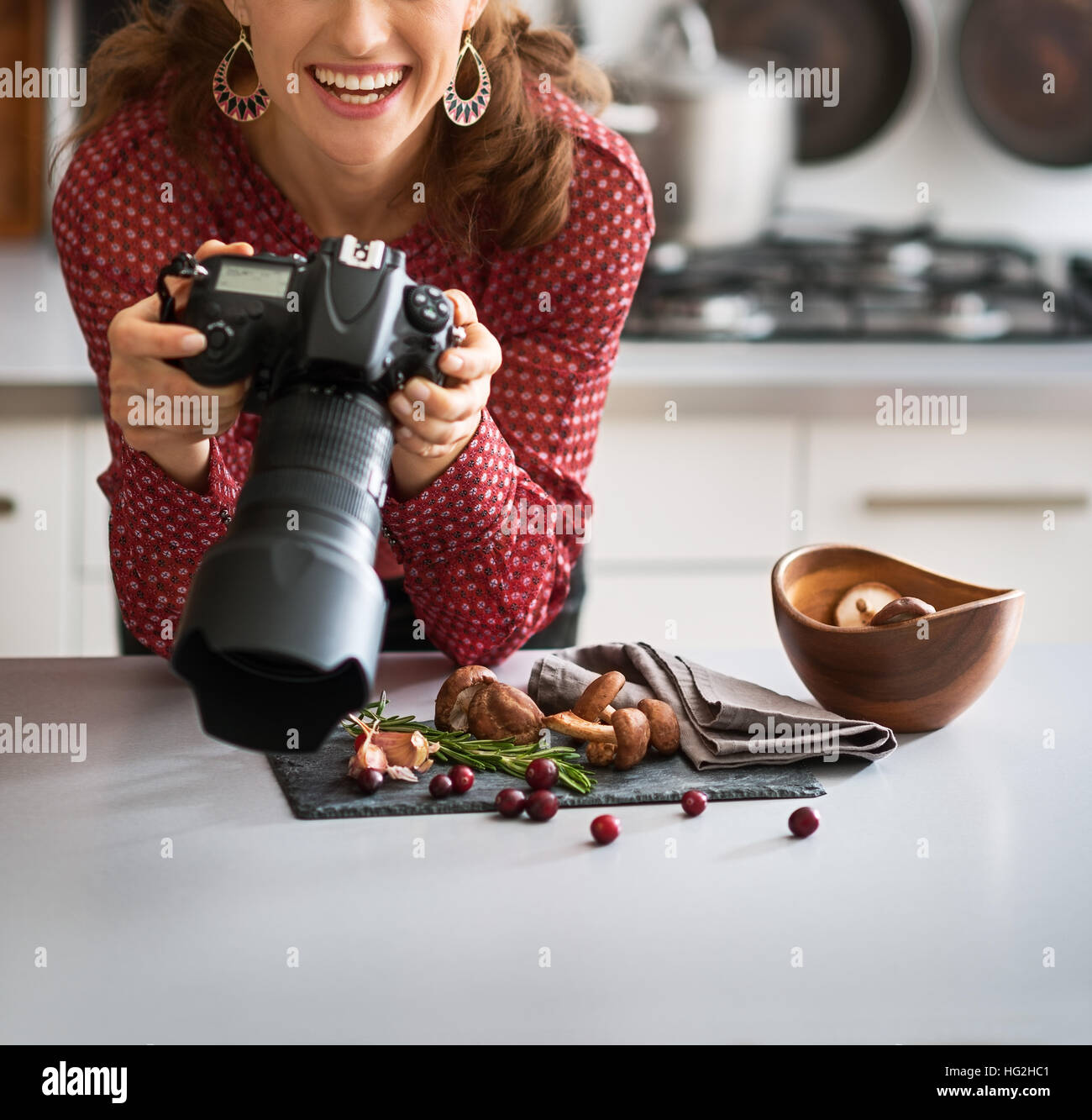 Una donna fotografo alimentari guarda fino dalla sua fotocamera, sorridente e felice. Ella è in una moderna cucina, fotografando autunno frutta e verdura - mushro Foto Stock