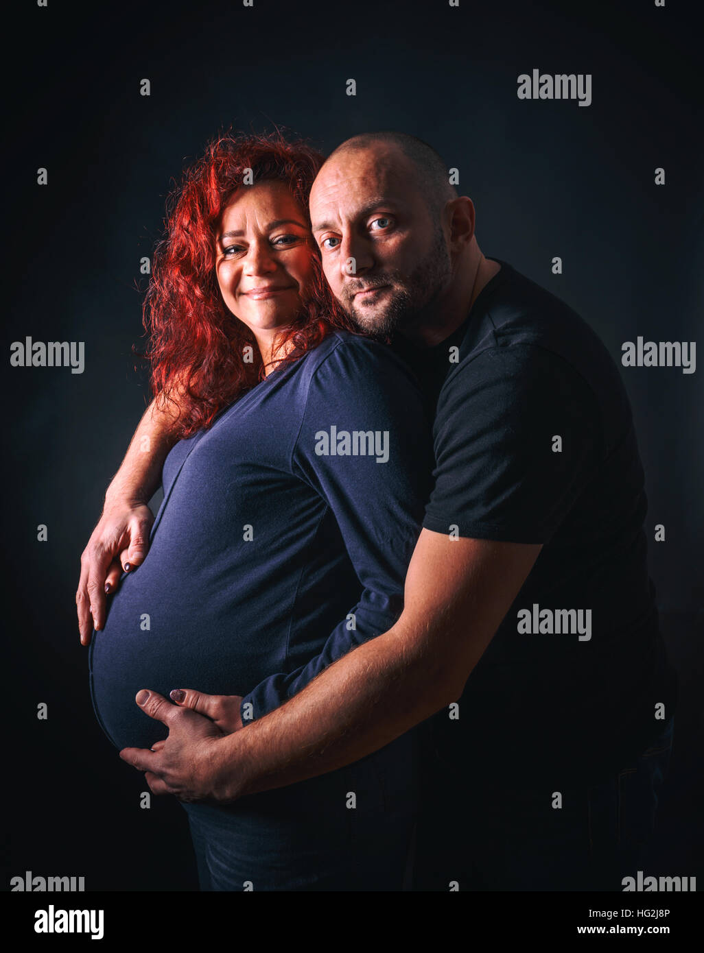 Donna incinta con il marito su sfondo scuro Foto Stock