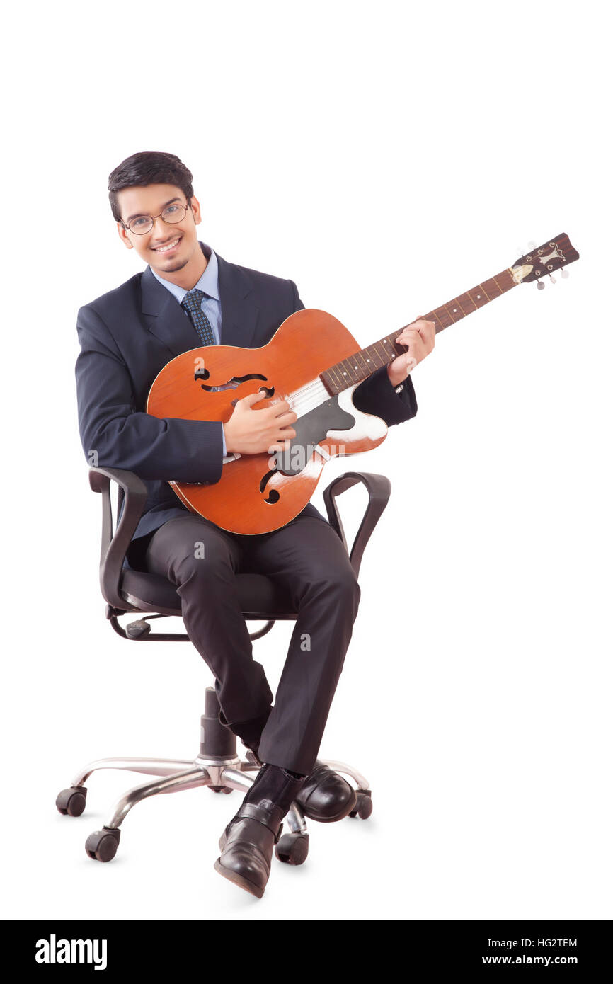Sorridente giovane uomo in abiti formali a suonare la chitarra, seduti su una sedia girevole contro uno sfondo bianco Foto Stock