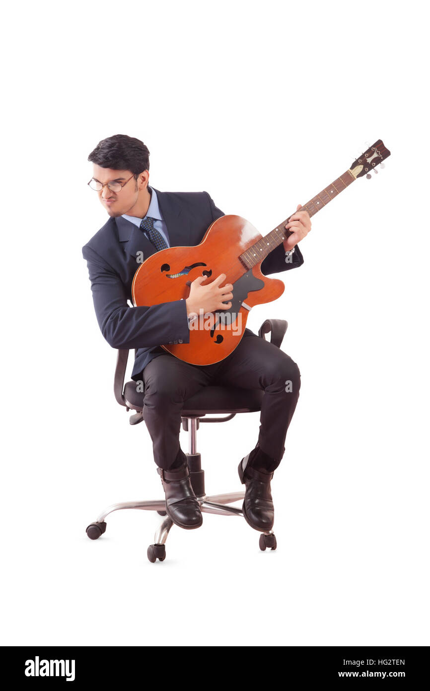 Giovane uomo in abiti formali a suonare la chitarra appassionatamente seduti sulla poltrona girevole contro uno sfondo bianco Foto Stock