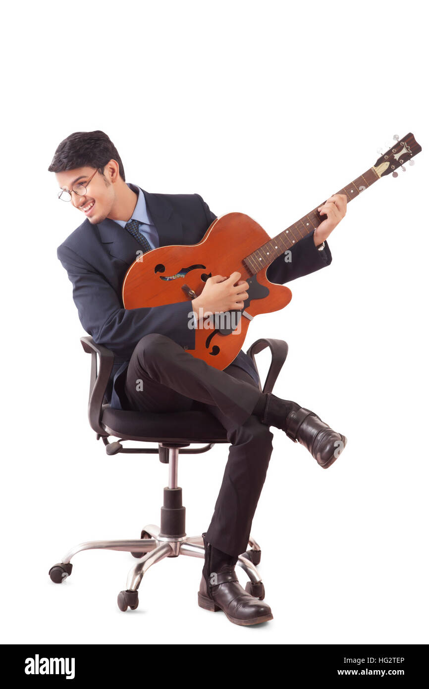 Sorridente giovane uomo in abiti formali a suonare la chitarra, seduti su una sedia girevole contro uno sfondo bianco Foto Stock