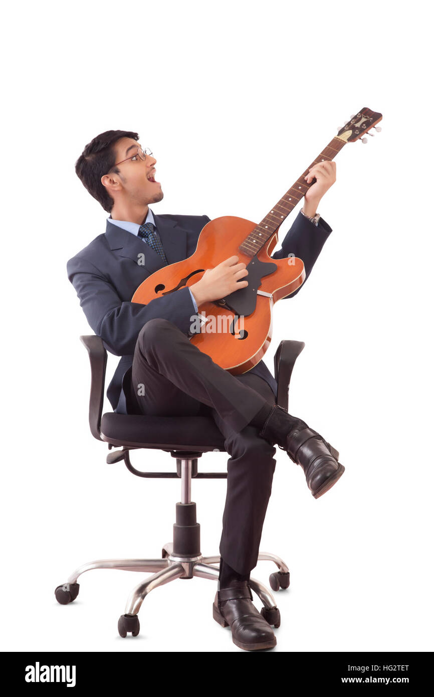 Giovane uomo in abiti formali a suonare la chitarra e cantare, seduti su una sedia girevole contro uno sfondo bianco Foto Stock