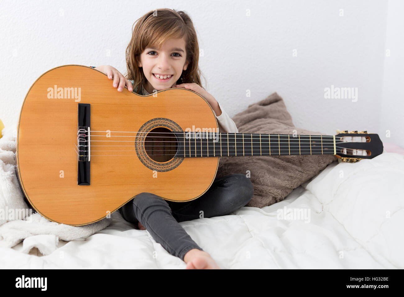 Bambina di imparare a suonare la chitarra classica, seduta sul suo letto  Foto stock - Alamy