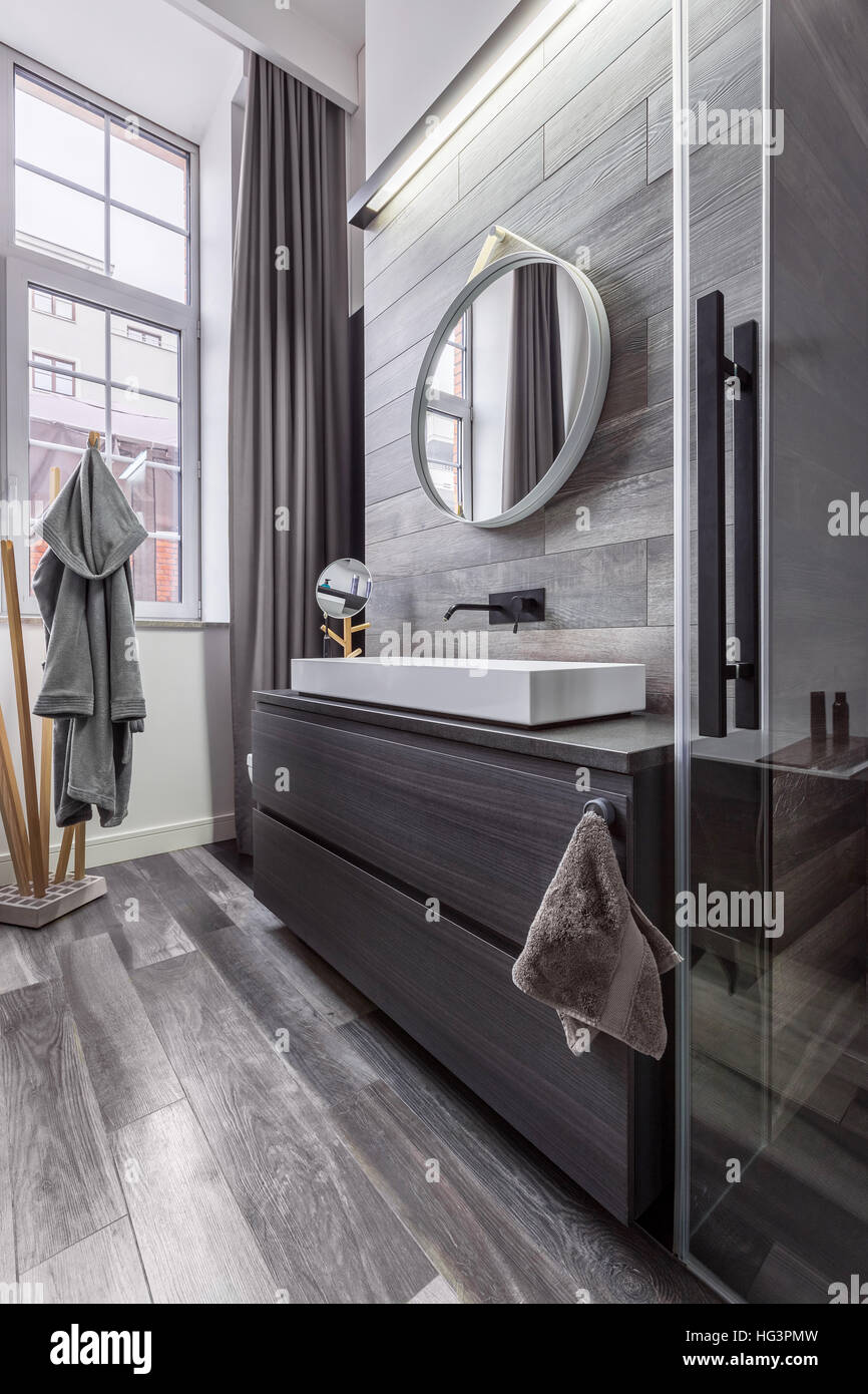 Elegante bagno in legno con specchio rotondo e bacino del piano del banco Foto Stock