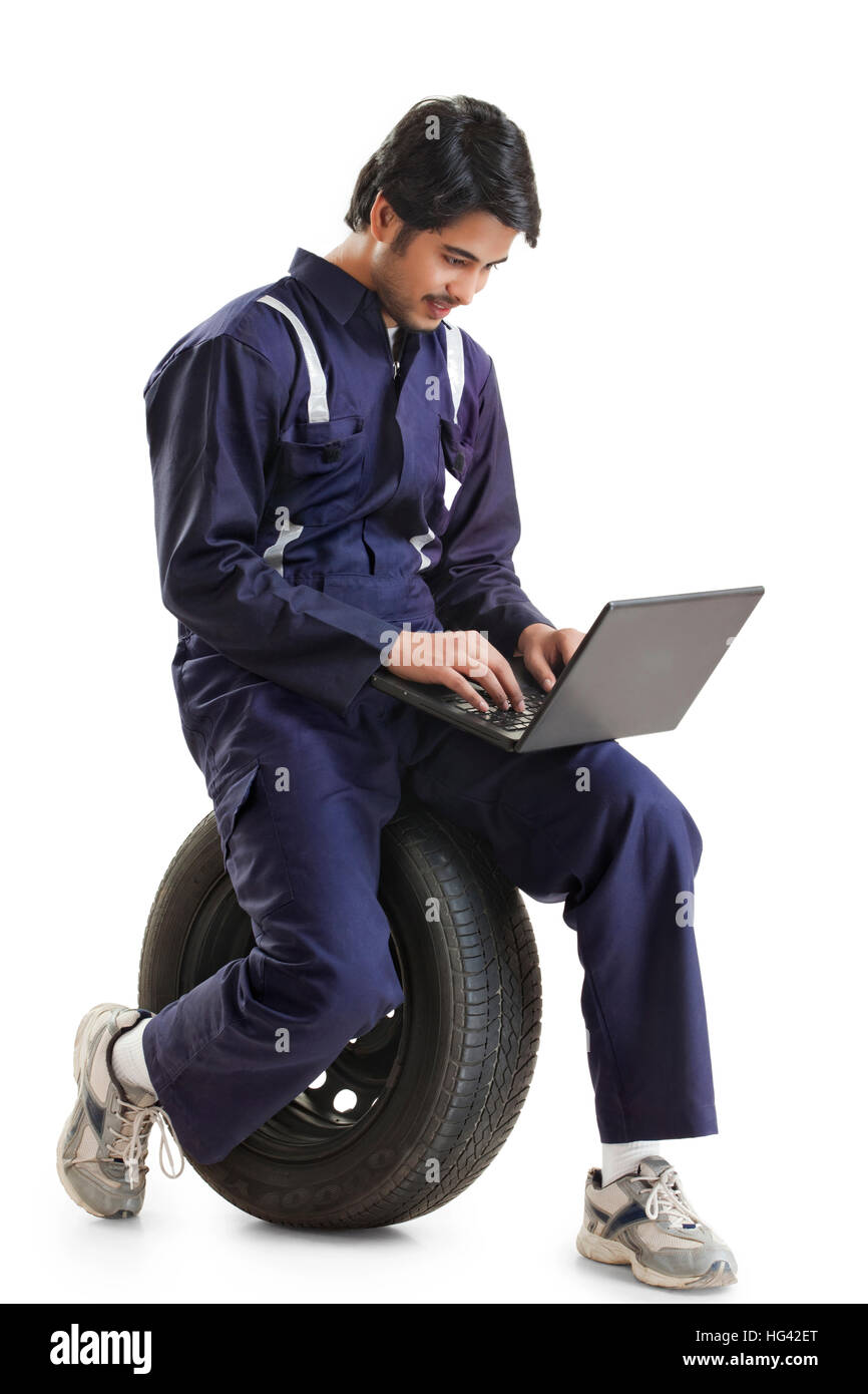 Autofficine seduti sul pneumatico e utilizzando computer portatile Foto Stock