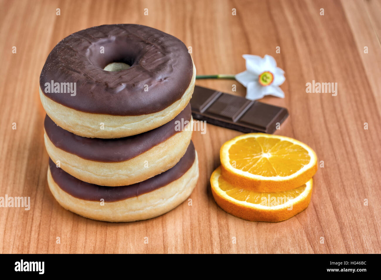 Tre le ciambelle con cioccolato fondente e fettine di arancia su una base di legno Foto Stock
