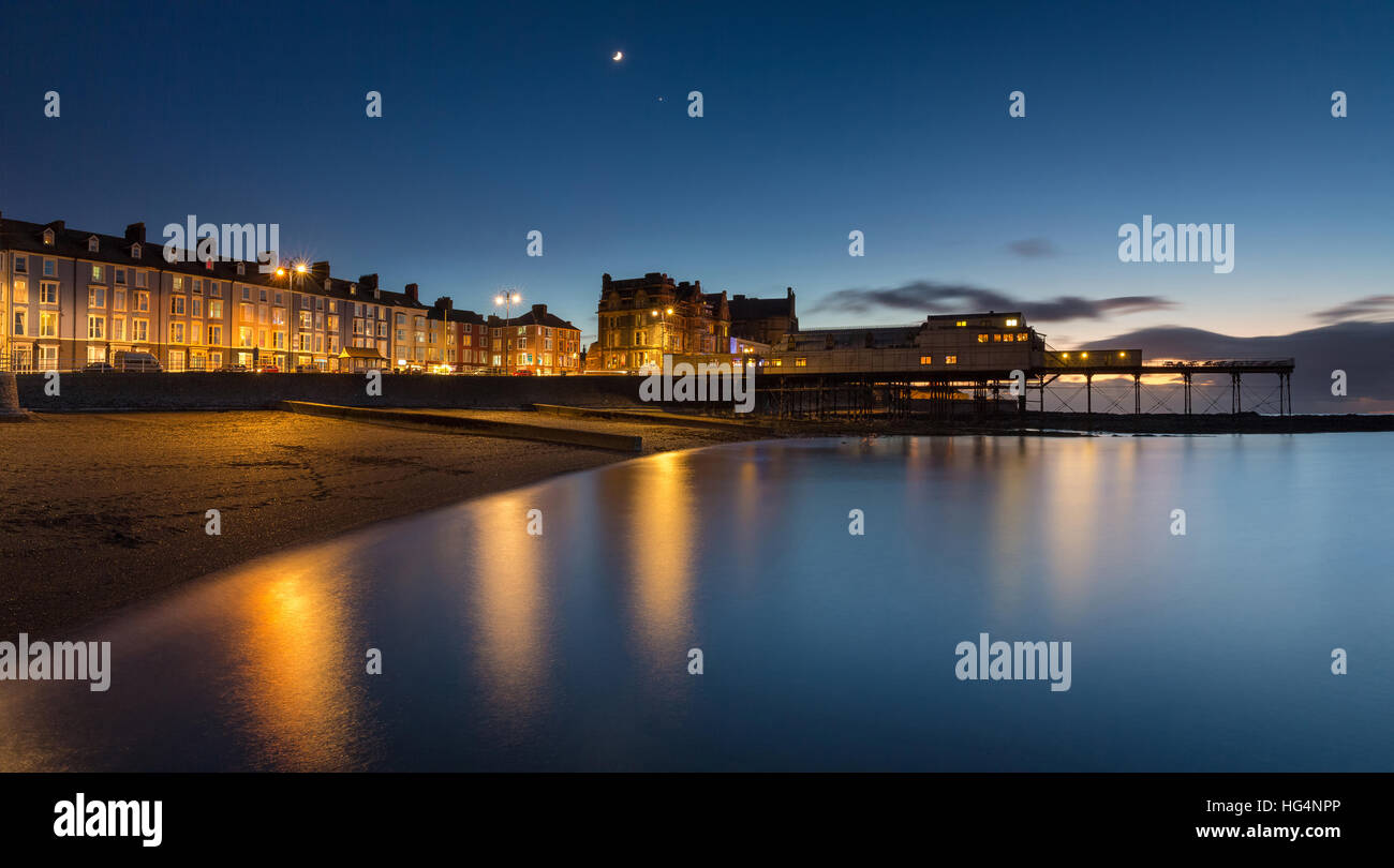 Aberystwyth promenade edifici e Pier in prima serata. Una falce di luna e il pianeta Venere raffigurato. Ceredigion, Wales, Regno Unito Foto Stock