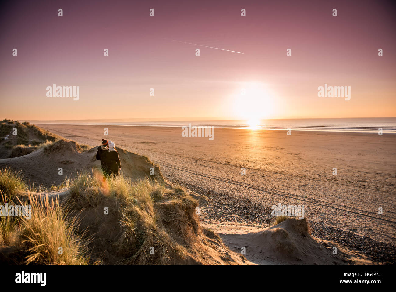 Un giovane su una spiaggia guardando verso il tramonto in inverno Foto Stock
