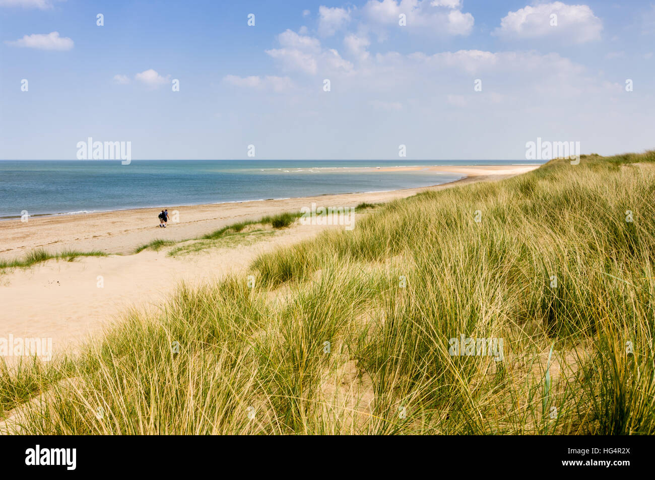 Due persone con zaini che camminano lungo una spiaggia di sabbia in una soleggiata giornata di primavera a Burnham Overy Staithe, Norfolk, Inghilterra, Regno Unito. Foto Stock