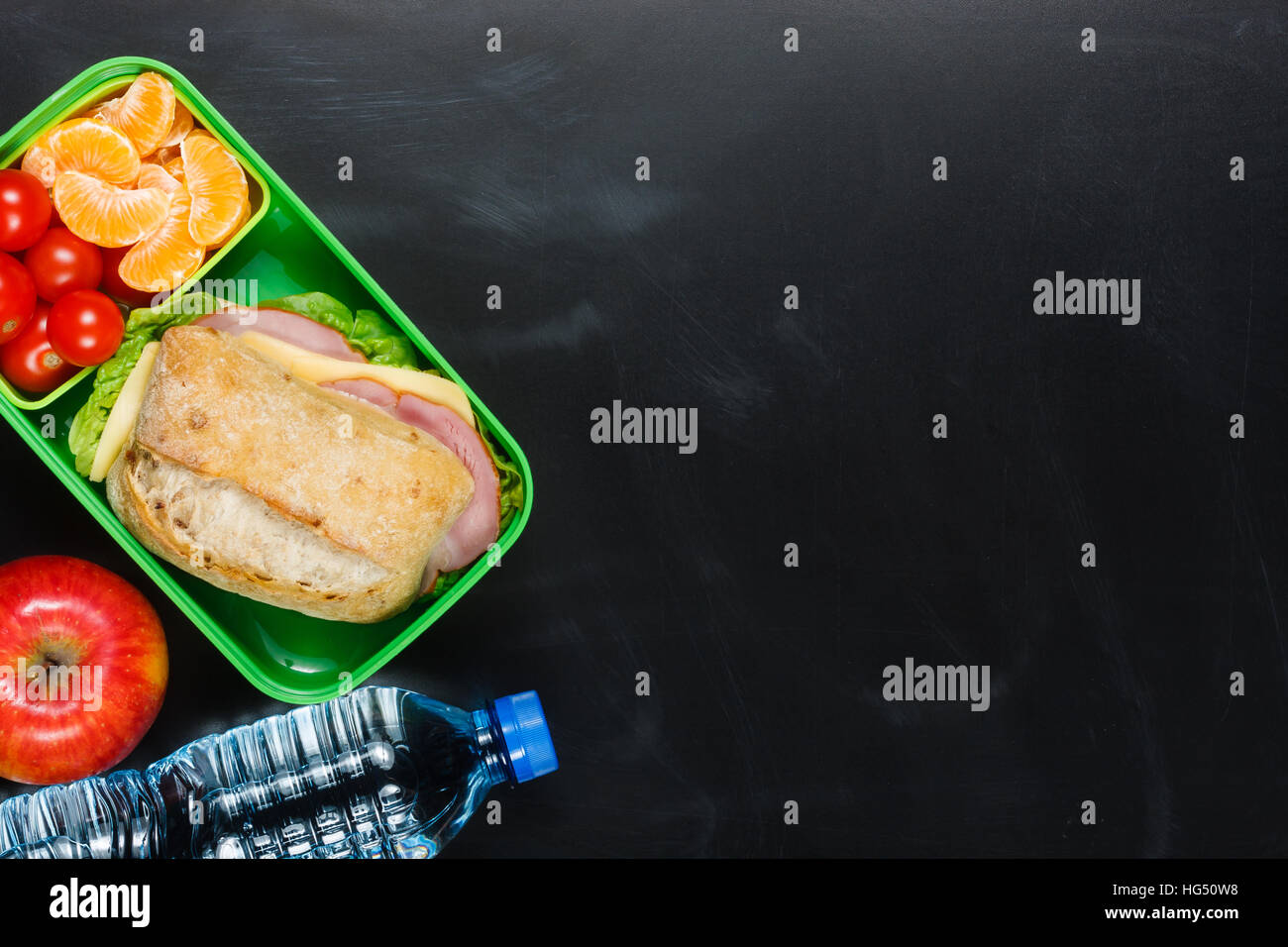 Sandwich, pomodorini, mandarino, Apple in plastica scatola di pranzo e una bottiglia di acqua sulla lavagna. Foto Stock