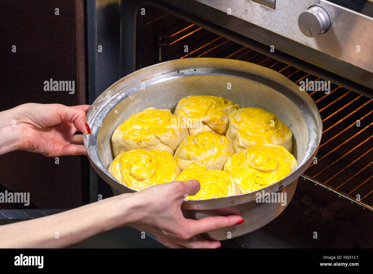 Giovane donna la cottura a casa tradizionale pane di festa. Ella mise il vassoio in forno caldo. Foto Stock