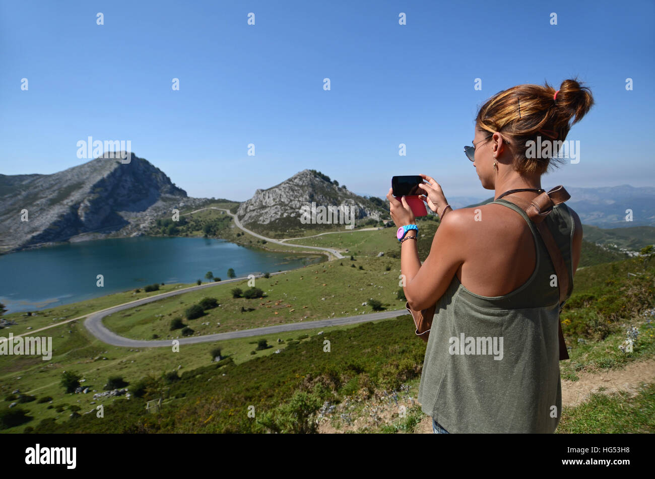 Giovane donna prende una foto dei laghi di Covadonga (Lagos de Covadonga) con il suo telefono cellulare Foto Stock