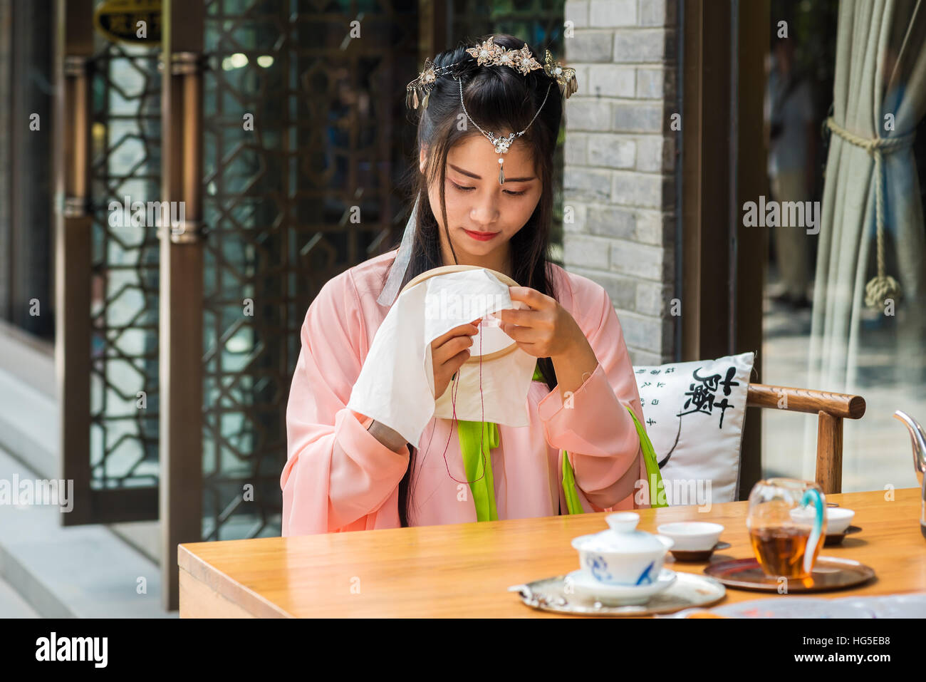 Chengdu, nella provincia di Sichuan, in Cina - Settembre 24, 2016 : ragazza cinese di indossare abiti tradizionali a una tabella con un po' di tessitura tè in una strada. Foto Stock