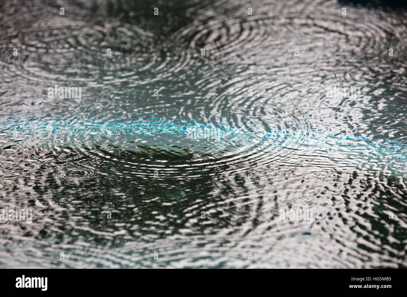 Gocce di pioggia caduta in un corpo di acqua la creazione di schizzi e anelli Foto Stock