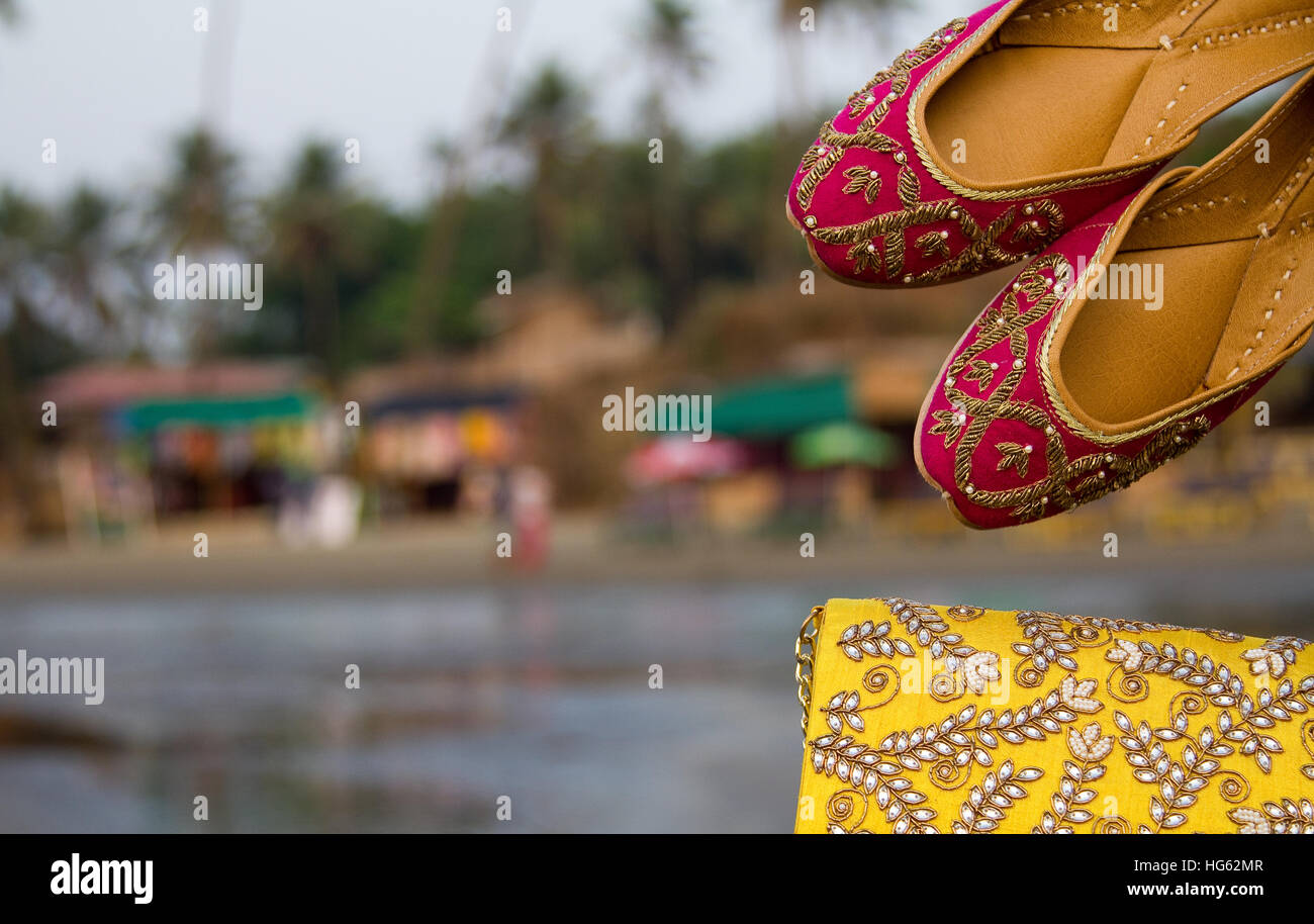 Coppia di tradizionale etnica indiana jutis rosa (scarpe donna) e una borsetta su una spiaggia in Goa, India con uno sfondo sfocato Foto Stock