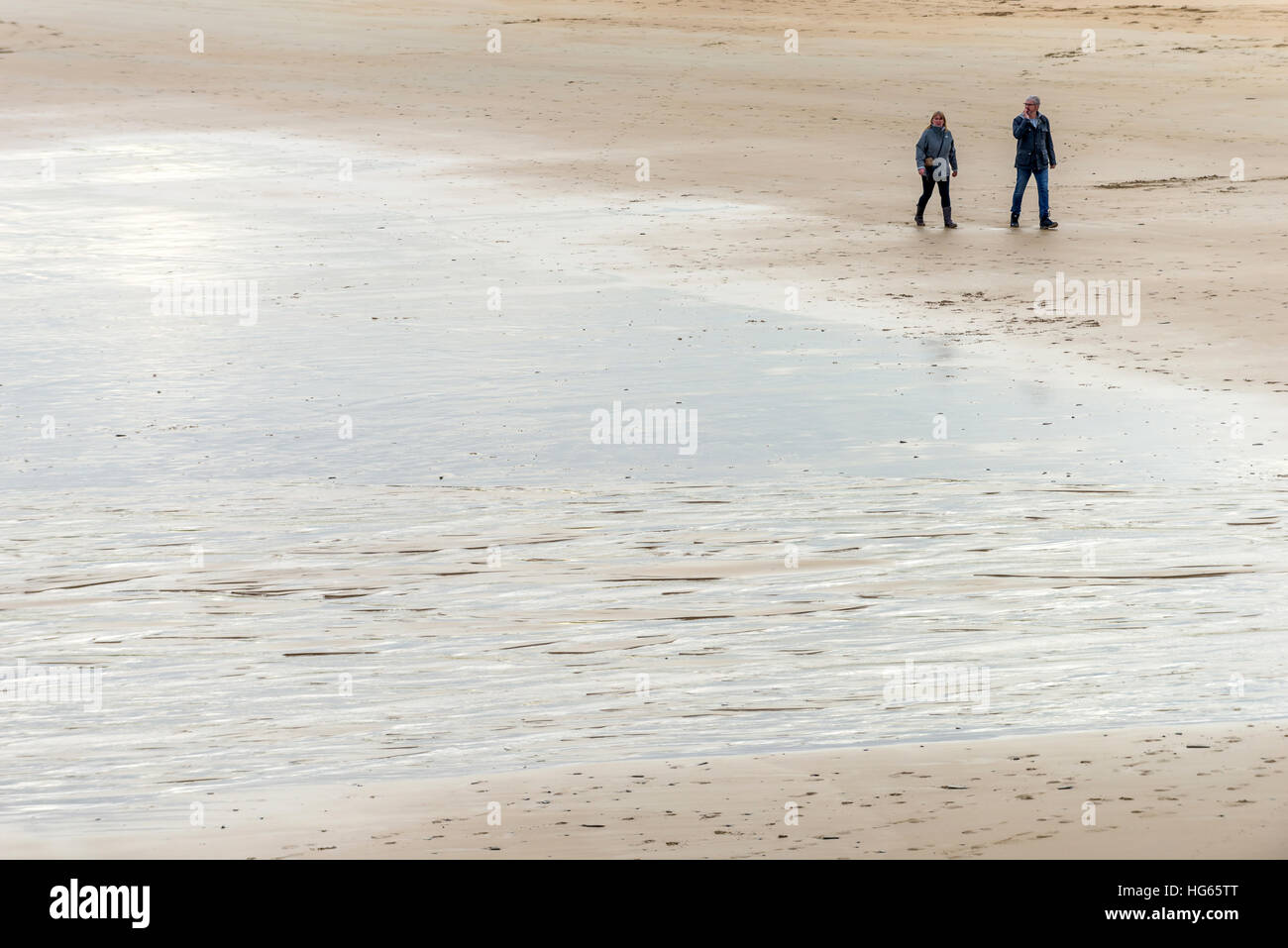 Due persone di passeggiata a bassa marea lungo il bordo del Camel Estuary in Cornovaglia Foto Stock