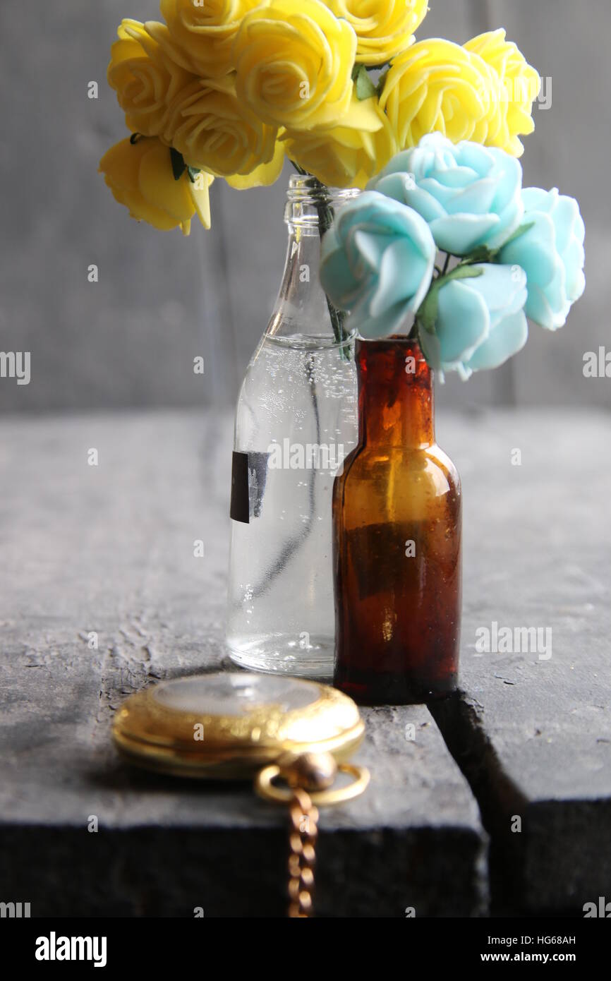 Fiori in bottiglie in legno tavolo vintage e golden pocket watch. Foto Stock