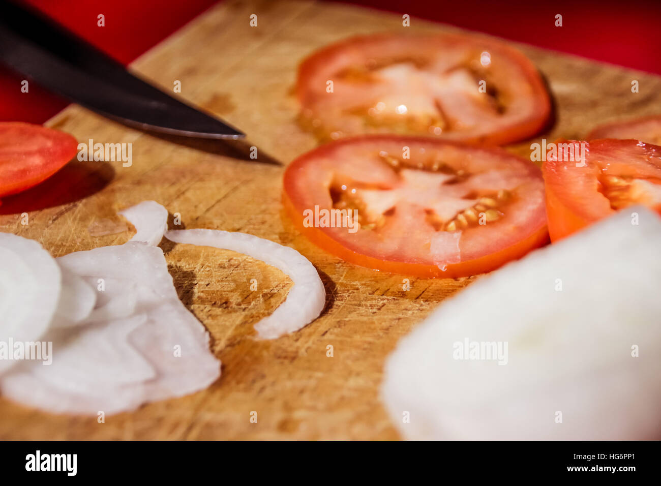 Fotografia di un coltello, le fette di pomodoro e cipolla in un legno tagliere Foto Stock