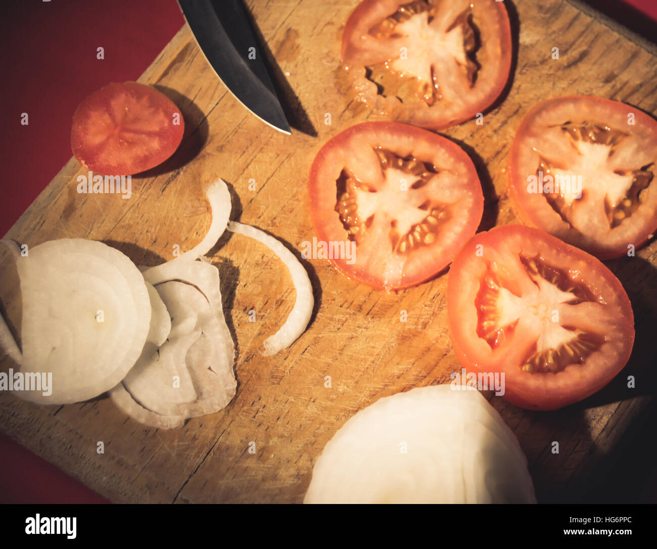 Fotografia di un coltello, le fette di pomodoro e cipolla in un legno tagliere Foto Stock