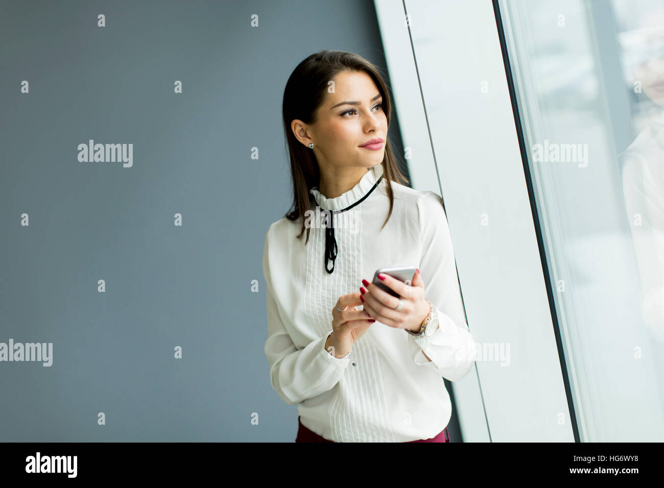 Piuttosto giovane donna con il cellulare da muro grigio in ufficio Foto Stock