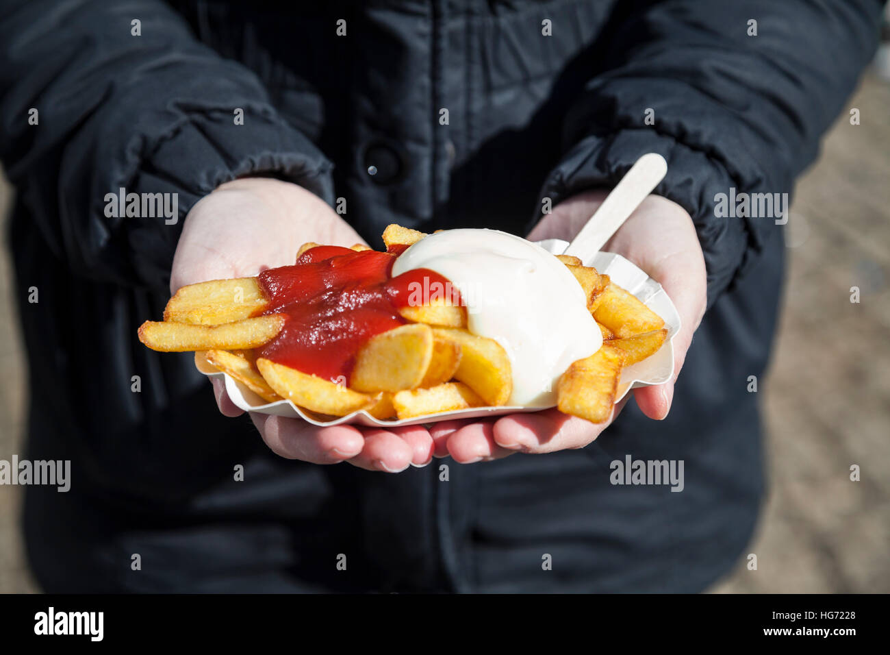 Donna che mantiene patate fritte con ketchup e maionese in mano Foto Stock