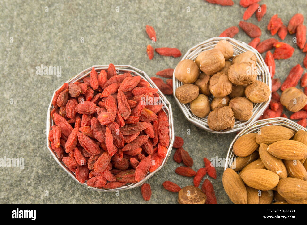 Bacche di Goji in una ciotola con le mandorle e le nocciole su sfondo rustico Foto Stock