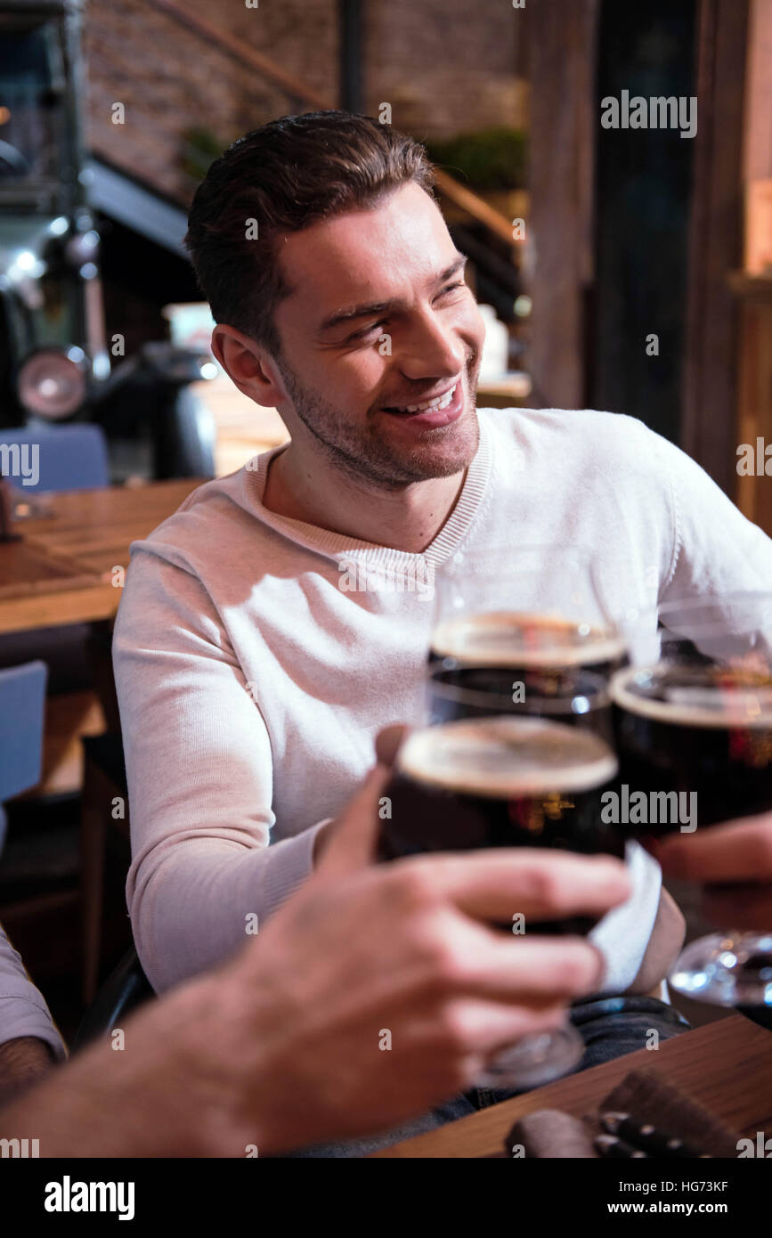 Piacevole uomo sorridente a bere con i suoi amici Foto Stock