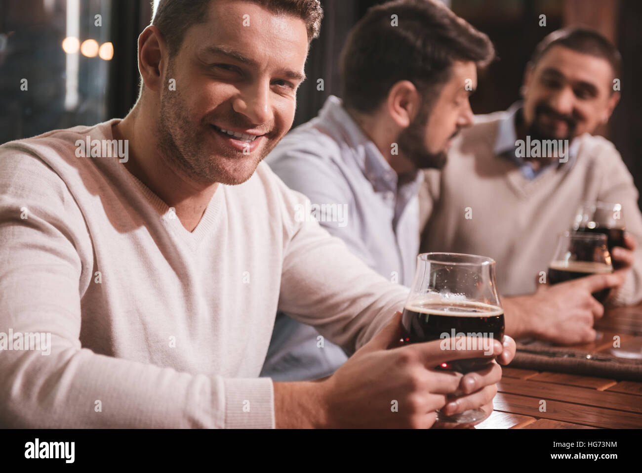 Attraente uomo sorridente seduto con i suoi amici al tavolo Foto Stock