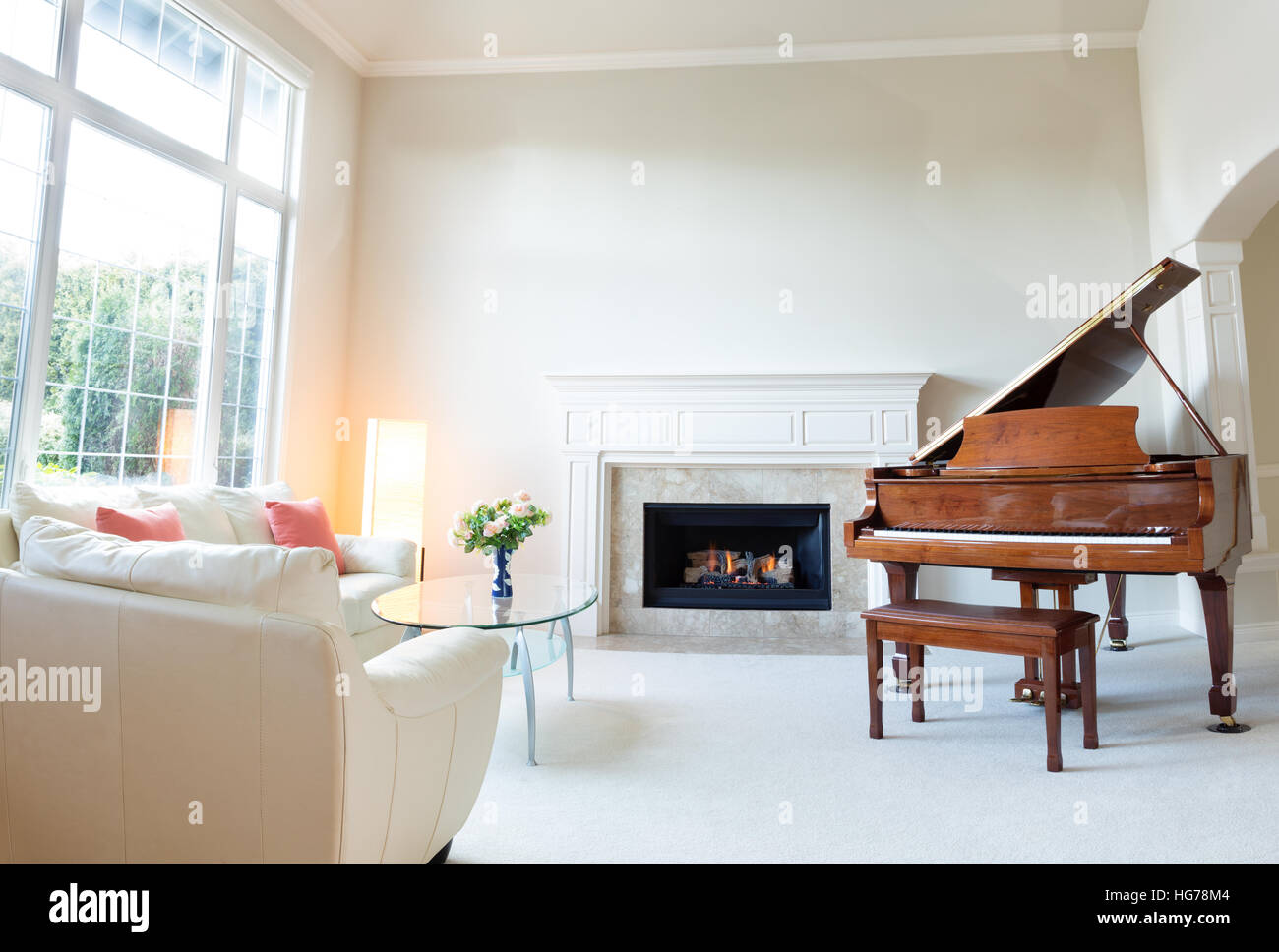 Brillante luce giorno entrata in soggiorno con caminetto, un pianoforte e con un divano in pelle bianca. Foto Stock