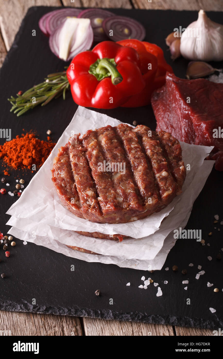 Materie di macinato di manzo hamburger di carne costolette di manzo con ingredienti sulla scheda. primo piano verticale Foto Stock