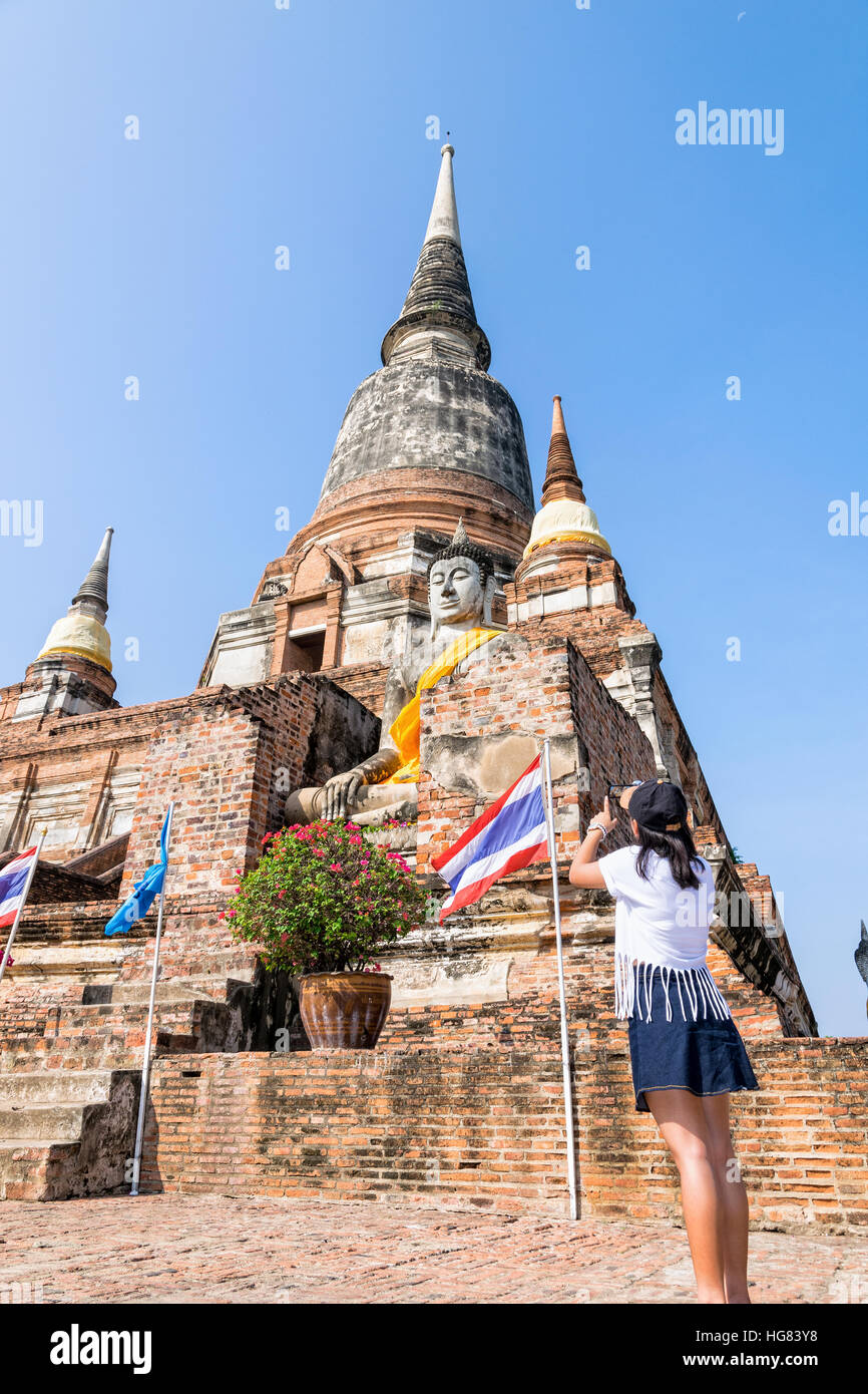Tourist ragazza adolescente in piedi prendere una foto di una statua del Buddha e antica pagoda in cielo blu sullo sfondo di Wat Yai Chaimongkol tempio Foto Stock