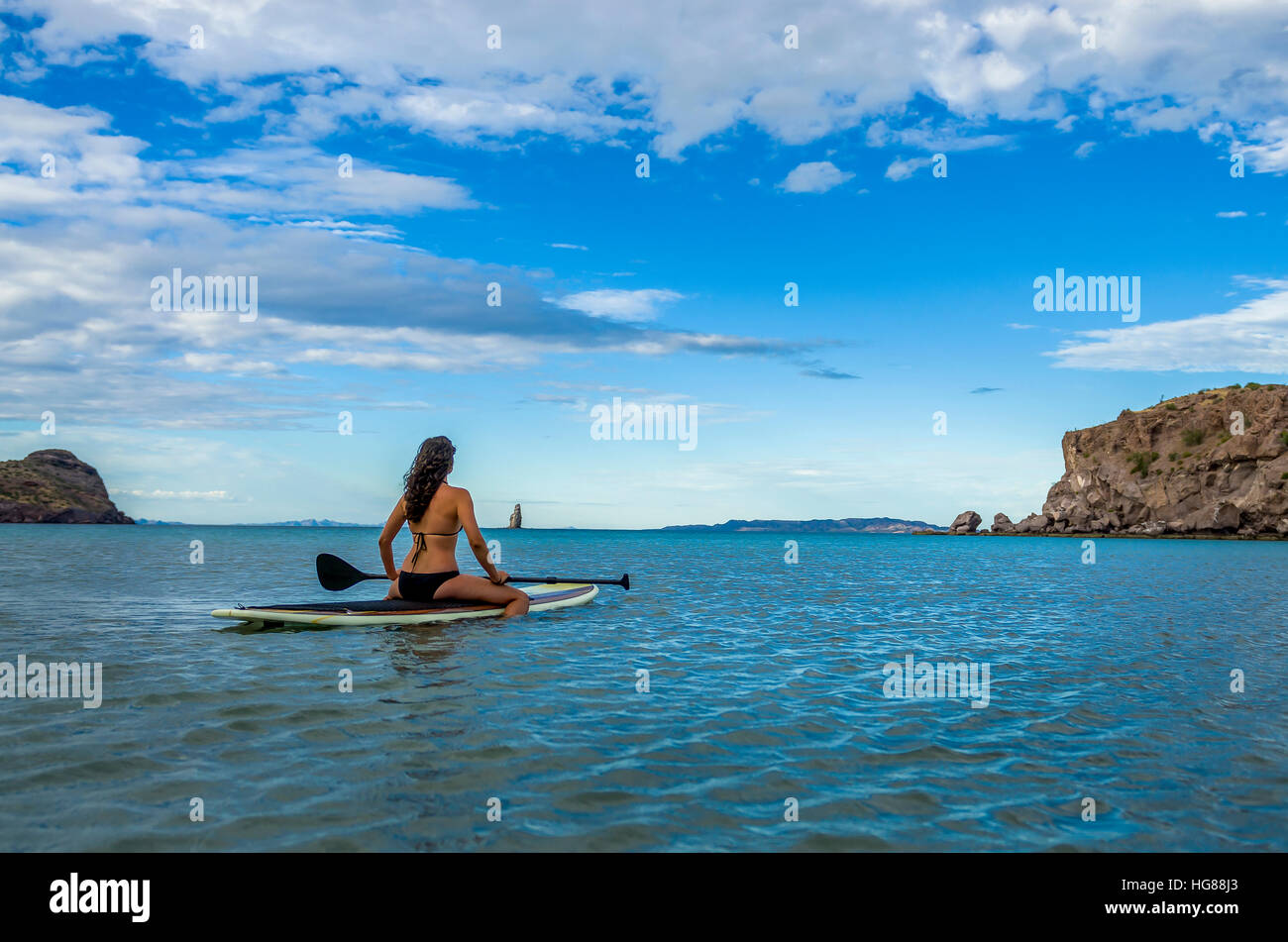 Donna seduta su paddleboard in mare contro il cielo blu Foto Stock