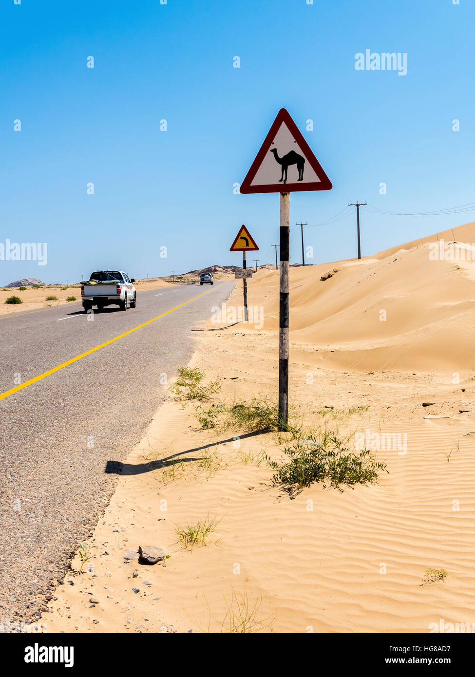 Strada attraverso il deserto sabbioso con segno di avvertimento del cammello di incroci, Ash Sharqiyah Sud, Oman Foto Stock