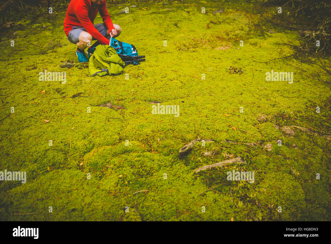 Sezione bassa di un escursionista con zaino accovacciato sul campo erboso Foto Stock