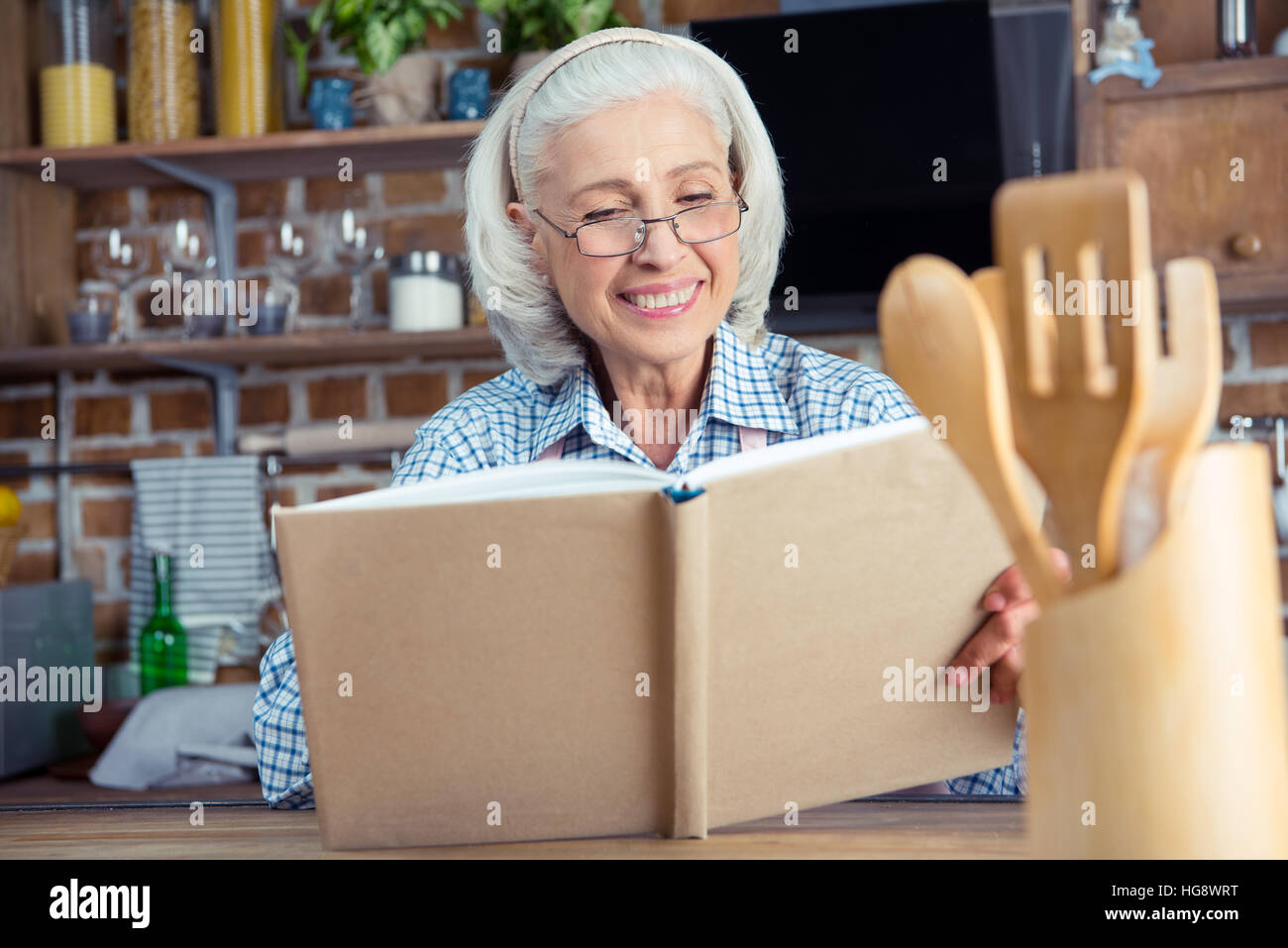 Sorridente donna senior in occhiali lettura cookbook in cucina Foto Stock