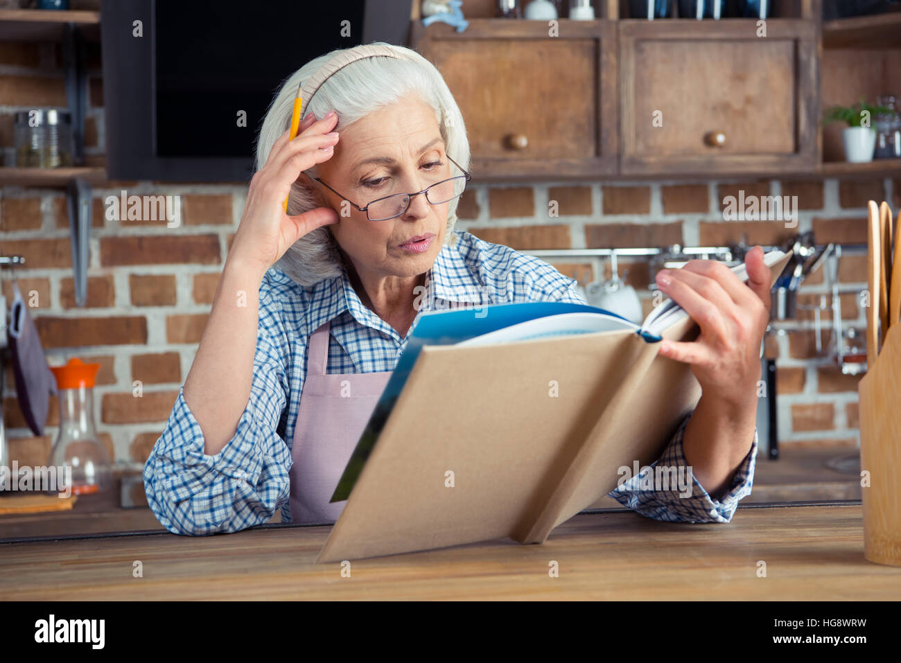 Donna Senior in occhiali lettura cookbook in cucina Foto Stock