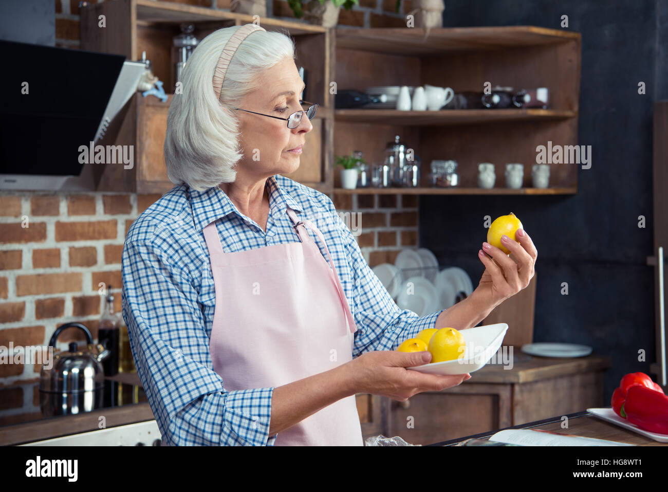 Donna Senior in occhiali e grembiule guardando i limoni in cucina Foto Stock